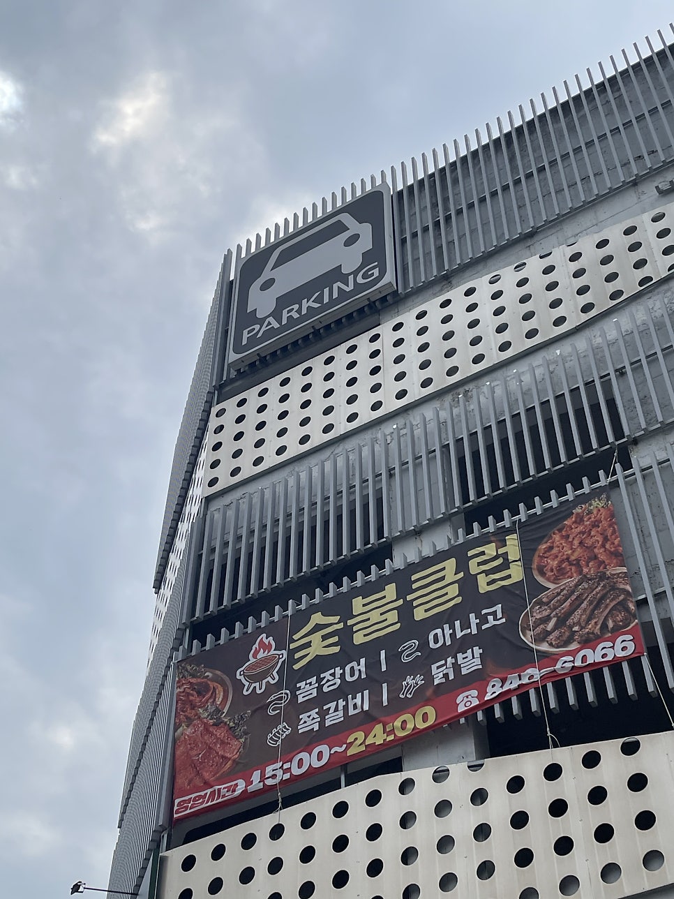 주차타워를 아래에서 올려다본 모습. 같은 건물에 다른 매장의 광고 현수막도 함께 걸려 있습니다.
