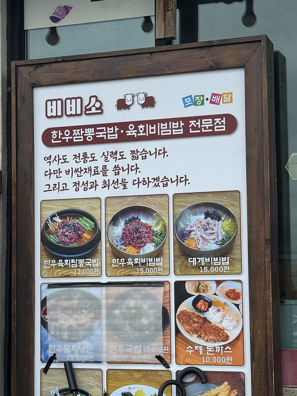 가게 앞 입간판. 한우육회짬뽕국밥·한우육회비빔밥·대게비빔밥 등 대표 메뉴와 가격, 그리고 비비소의 다짐이 함께 적혀 있다.
