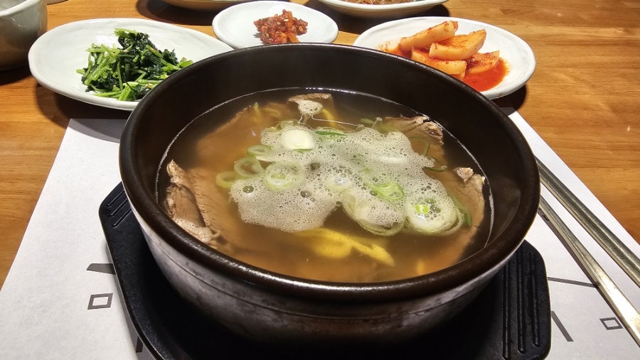 뚝배기에 담겨 나오는 한우곰탕. 대파와 고명을 얹은 맑은 국물에 나물·깍두기·김치가 곁들여집니다.