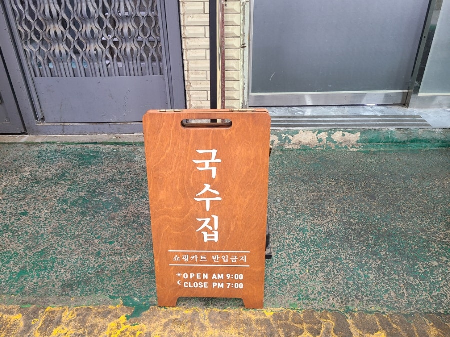 매장 앞 '국수집' 나무 팻말. 영업 안내 문구가 함께 붙어 있습니다.