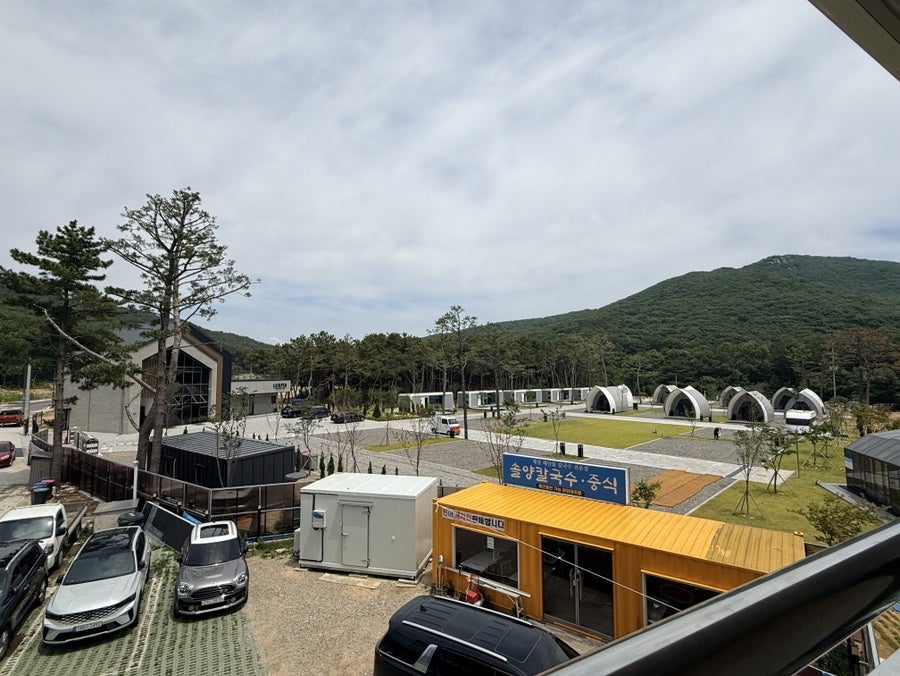 건물에서 내다본 주차장과 주변 풍경. 산과 나무로 둘러싸인 한적한 분위기입니다.