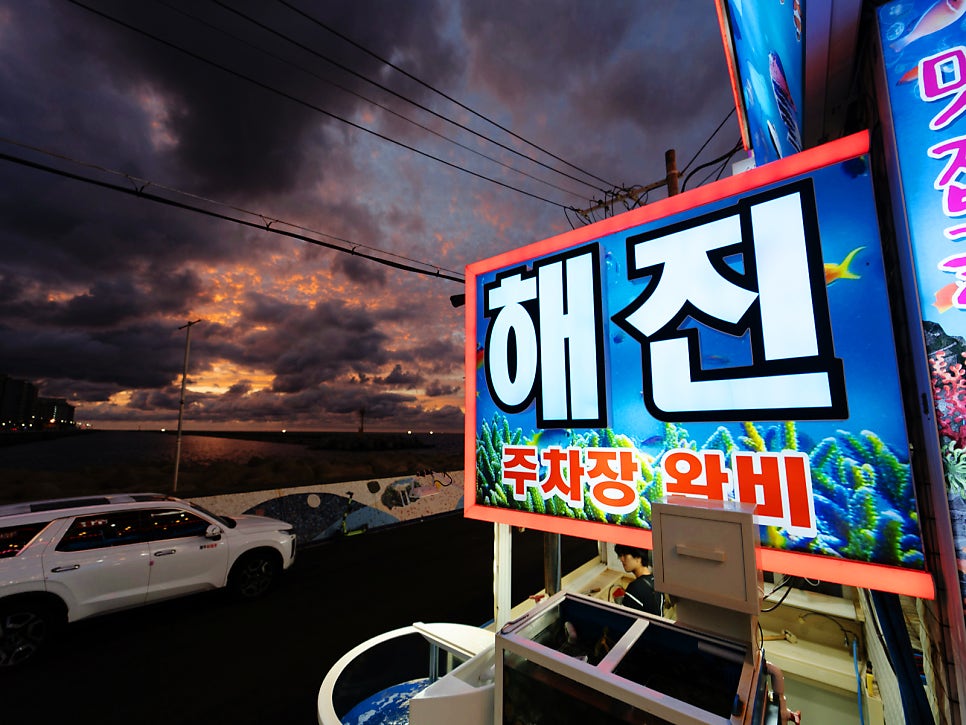 '주차장 완비' 문구가 적힌 간판과 서부두 하늘의 노을. 주차 걱정 없이 찾아갈 수 있습니다.