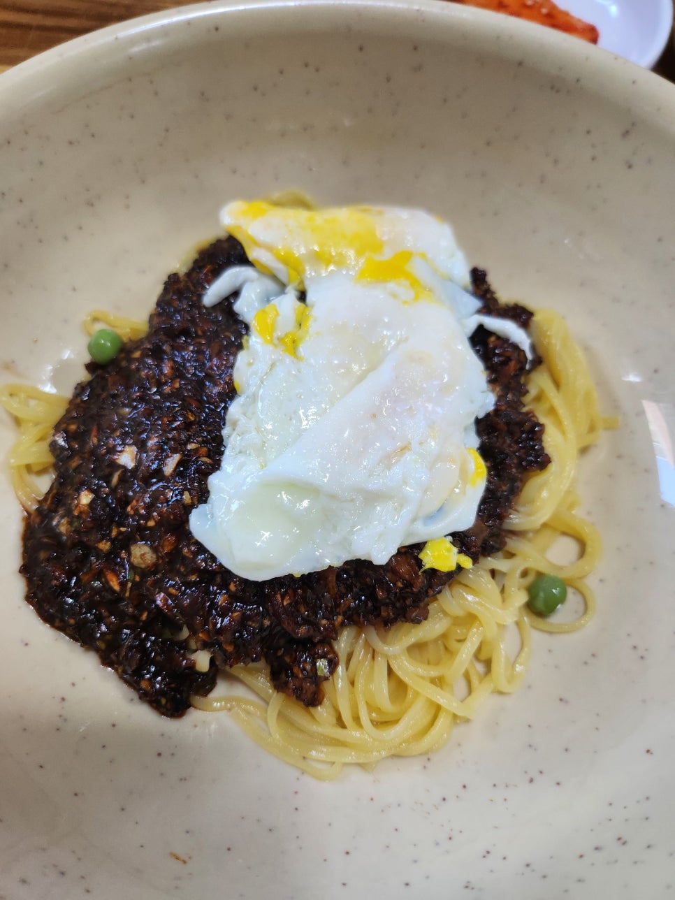 중깐 클로즈업. 얇은 면 위의 곱게 다진 고기 소스, 계란 노른자, 초록색 완두콩이 시각적으로 돋보입니다.