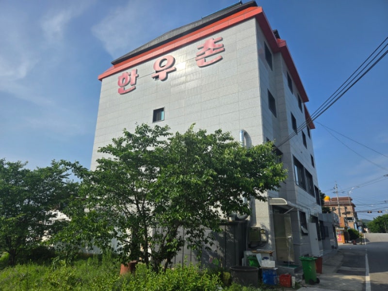 직판장 바로 옆, 실제로 구워 먹는 식당 건물. 벽면에 '한우촌' 글자가 크게 붙어 있어 멀리서도 눈에 띕니다.
