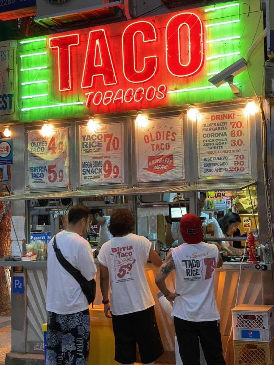 빨간 'TACO' 네온사인이 눈에 띄는 올디스타코 을지로 본점. 창구 앞으로 주문하려는 손님들이 줄을 서 있습니다.