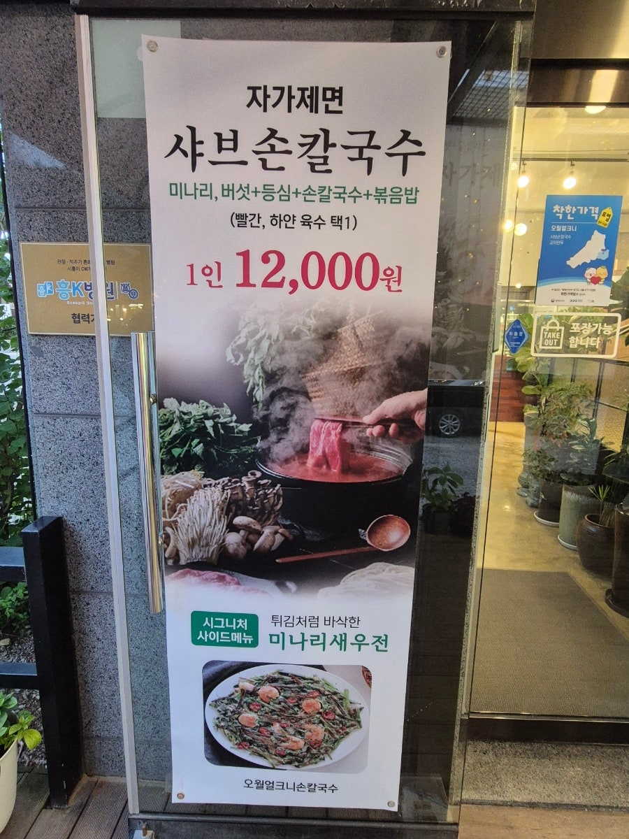 매장 입구의 메뉴 안내판. 자가제면 샤브손칼국수 1인 12,000원, 미나리새우전이 시그니처 사이드 메뉴로 적혀 있습니다.