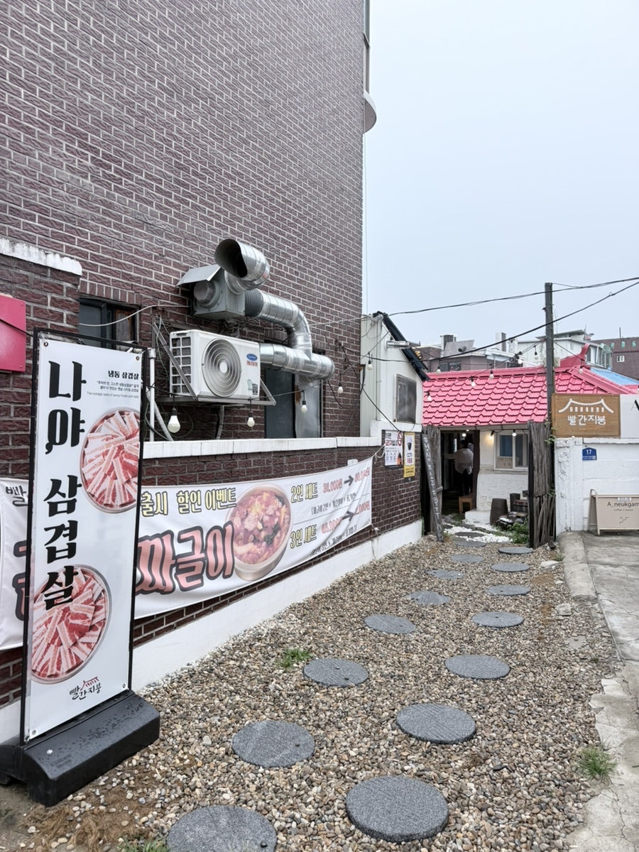 골목 안쪽 빨간지붕 입구. 냉삼과 김치짜글이 세트 이벤트 배너가 세워져 있습니다.