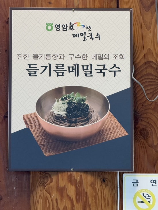 매장에 걸린 들기름메밀국수 메뉴 사진. 짙은 메밀면 위에 채소와 김가루를 올려 냅니다.